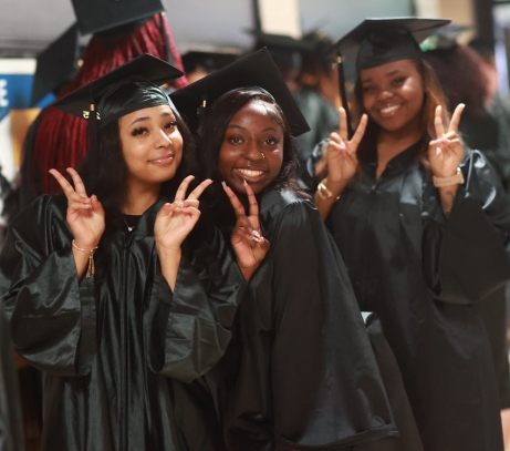 Three smiling graduates each holding up the peace sign