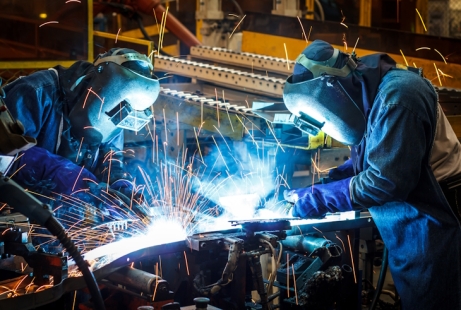 Two people wearing full welding gear using welding equipment